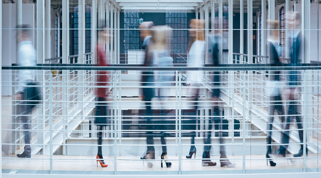 A panorama of blurred-out people walking in a corridor of a corporate office, going in different directions