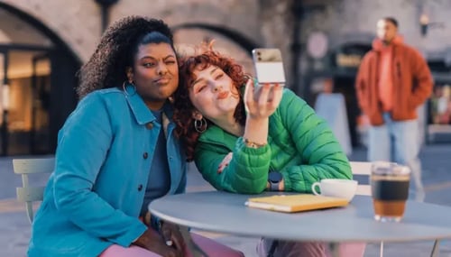 Two women happily taking a selfie outside a cafe, showcasing their friendship