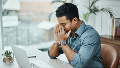 Man sitting on the work desk holding his face.