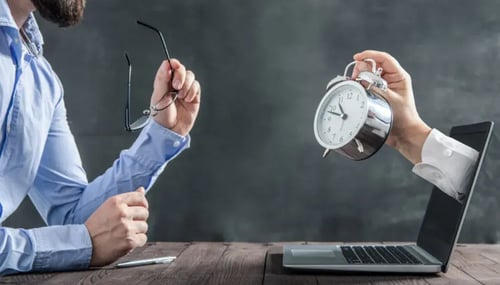 A man holds a clock in one hand and a laptop in the other, symbolizing the balance between time and technology