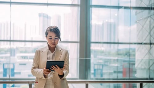 Professional woman standing in front of office window looking at tablet